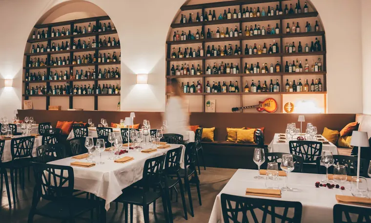 La sala di CLAP con la parete di bottiglie ad arco e i tavoli apparecchiati